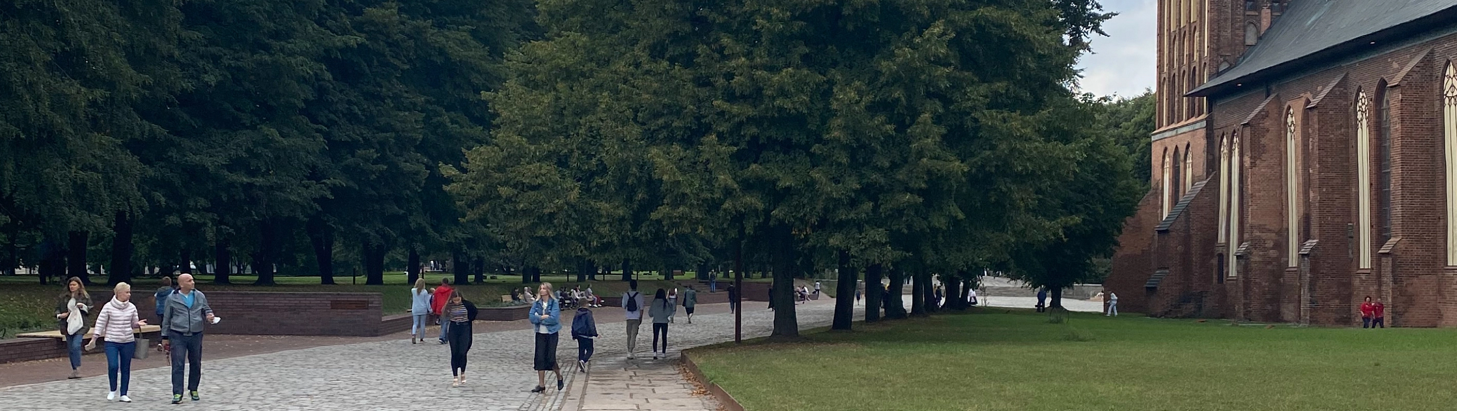 Люди гуляют по мощеной аллее у старинного кирпичного здания