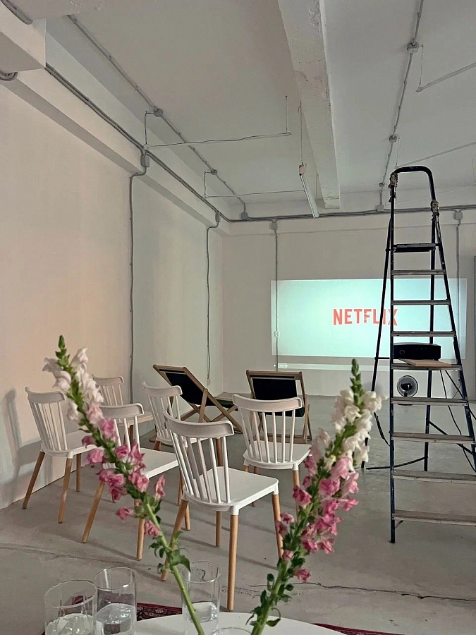 Зал для просмотра фильмов с белыми стенами, проектором и стульями, оформленный в индустриальном стиле.