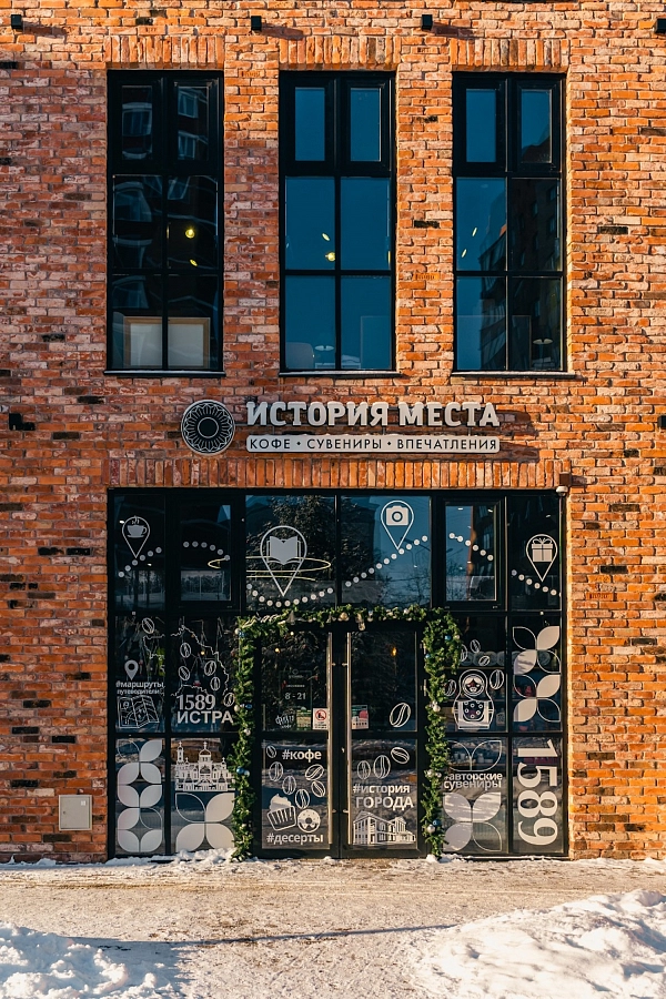 Фасад кофейни «История места» в кирпичном доме с большими окнами и праздничным оформлением.