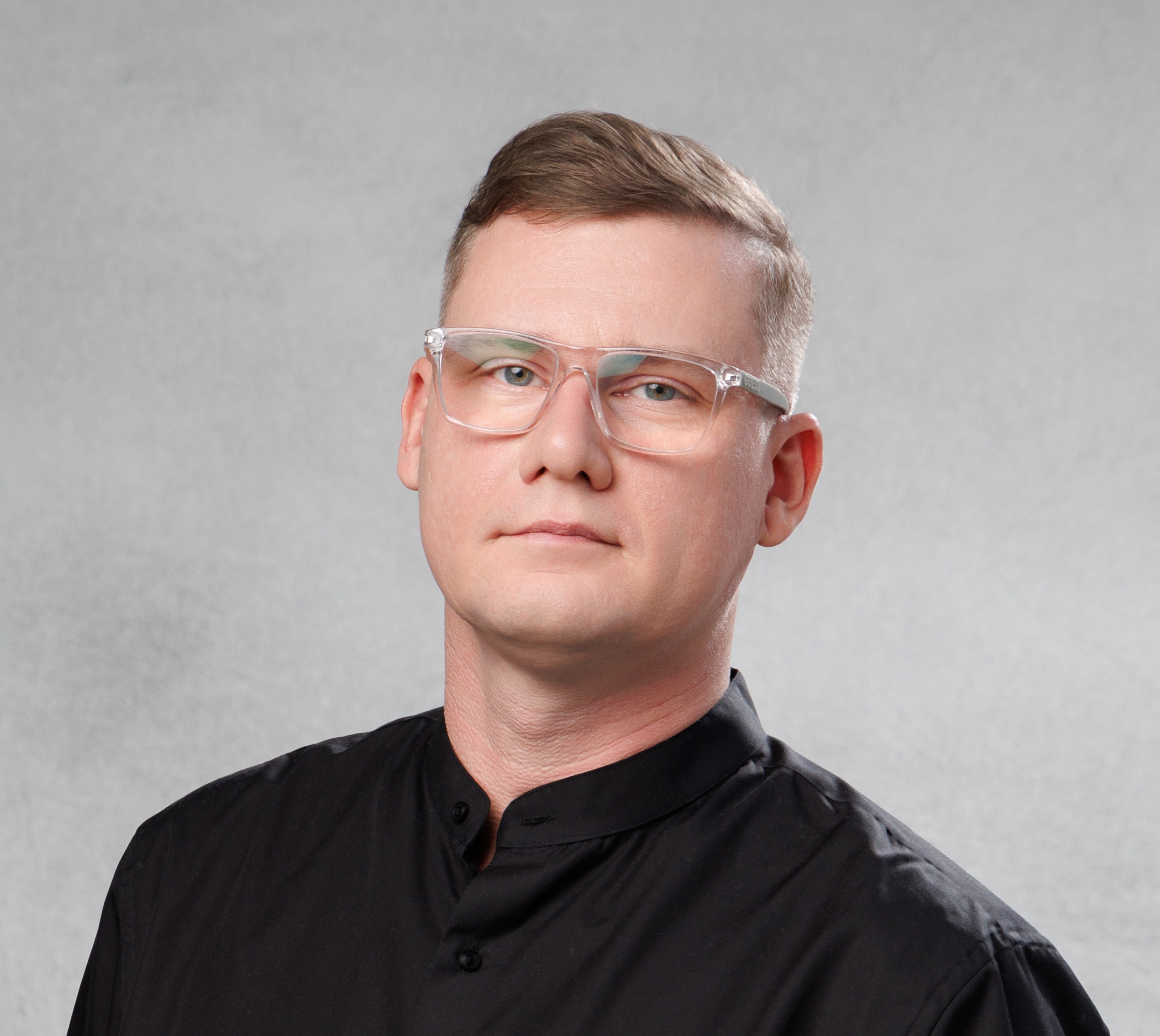 Портрет мужчины в очках и черной рубашке на светлом фоне, участник архитектурного сообщества