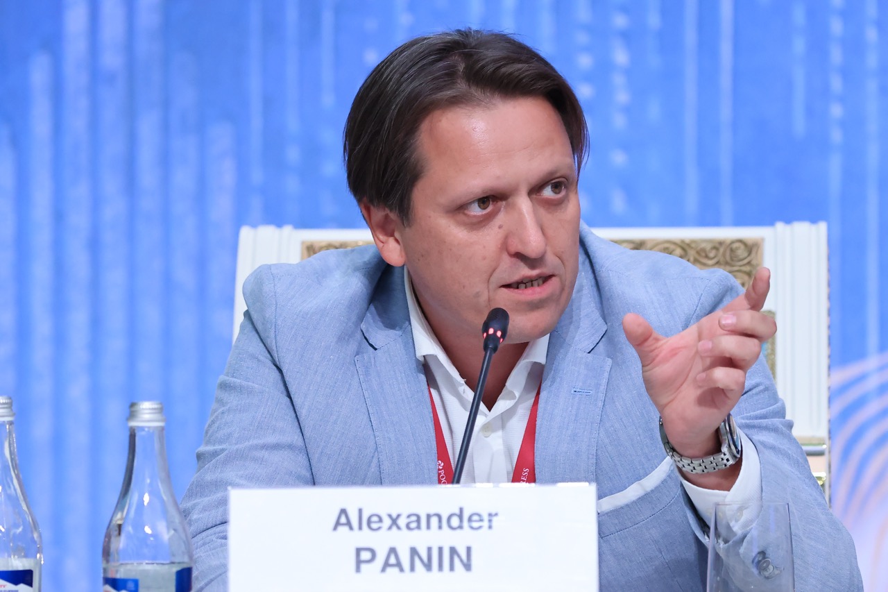 Мужчина в голубом пиджаке выступает на конференции, перед ним табличка «Alexander Panin»