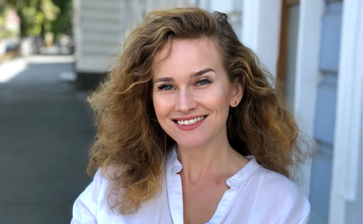 Портрет женщины с кудрявыми волосами в белой рубашке на фоне городской улицы