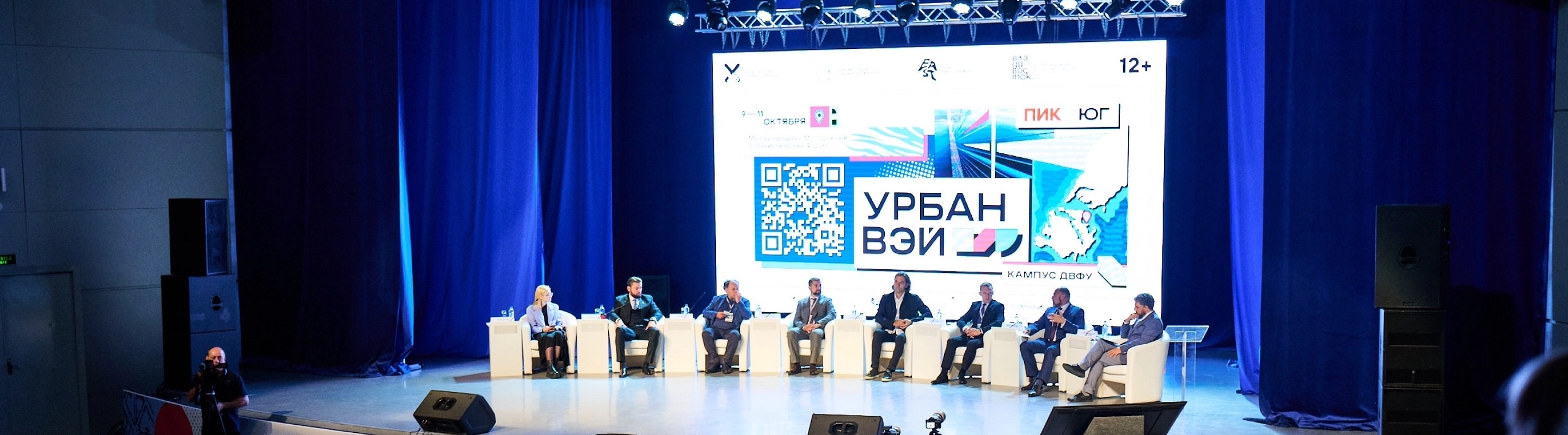 Панельная дискуссия на международном урбанистическом форуме «Урбанвэй» — спикеры на сцене и большой экран с логотипом события.