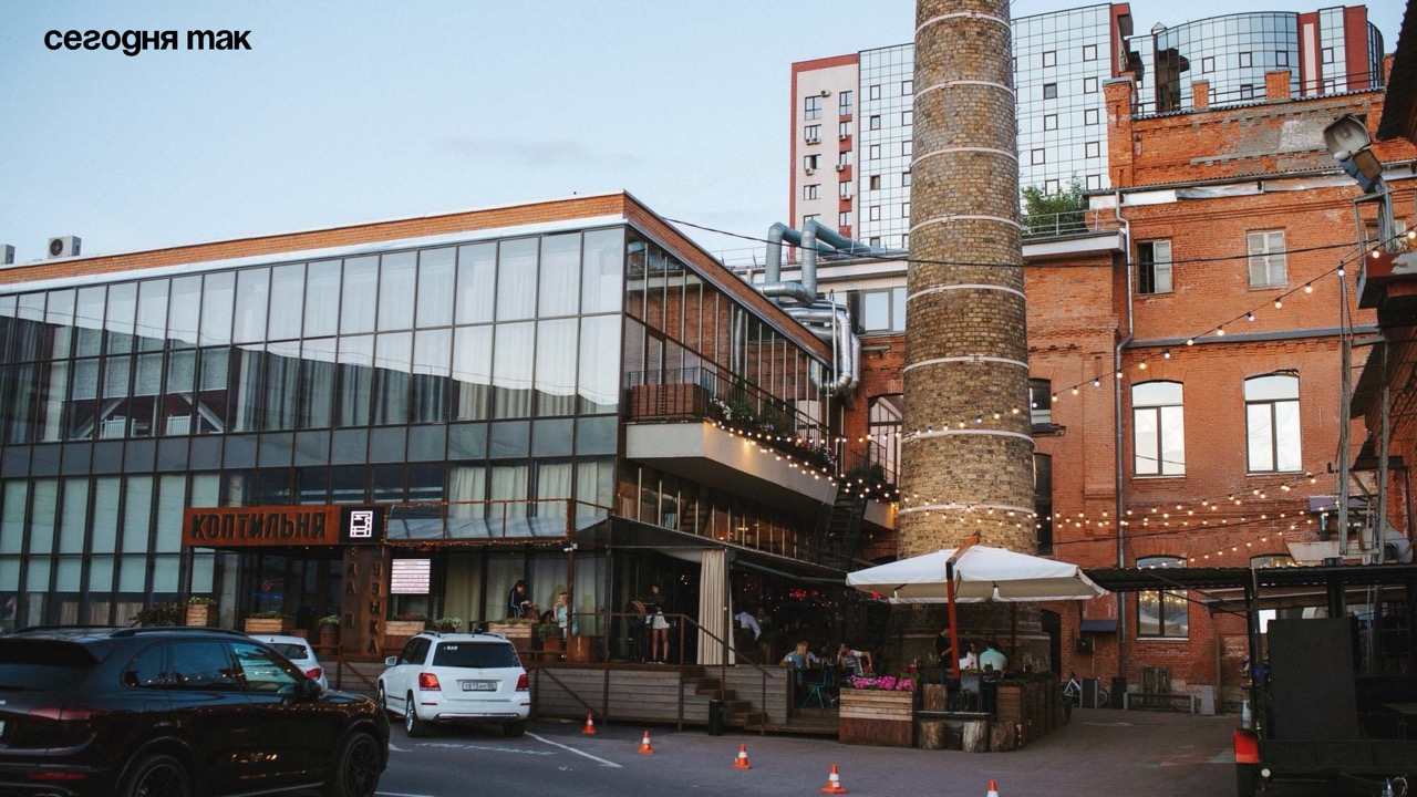 Современное здание из стекла и кирпича на фоне жилых домов и старой промышленной трубы