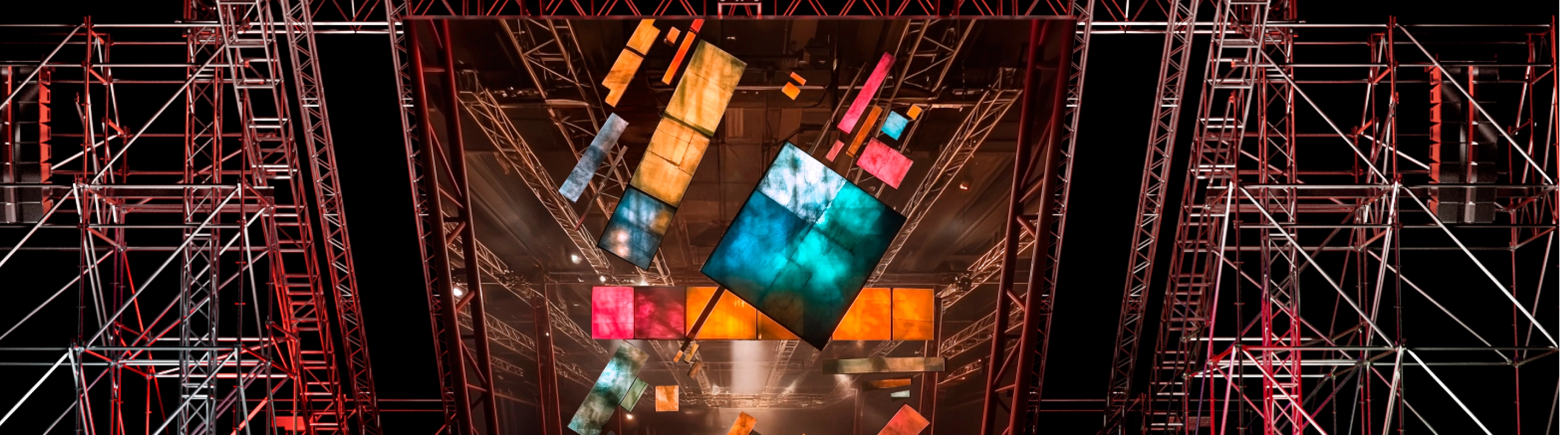 Сцена с подвесными разноцветными экранами и металлическими конструкциями на выставке или концерте.