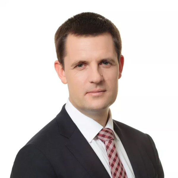 Портрет мужчины в тёмном костюме и клетчатом галстуке, снятый на белом фоне.