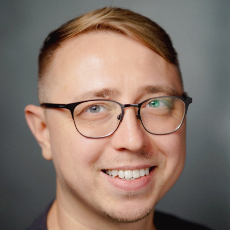 Мужчина в очках с улыбкой на сером фоне, участник архитектурного форума